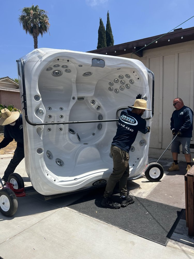 Crew lifting a hot tub spa in a San Diego backyard at golden hour